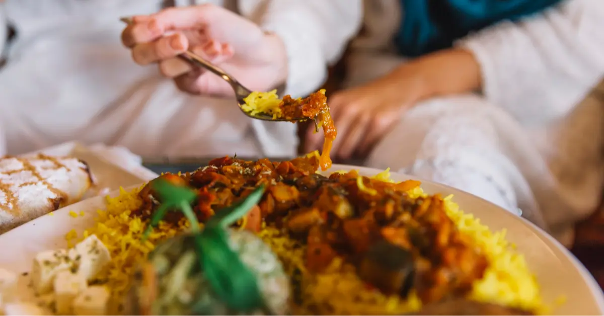 A woman serving herself biryani with a spoon during a gathering