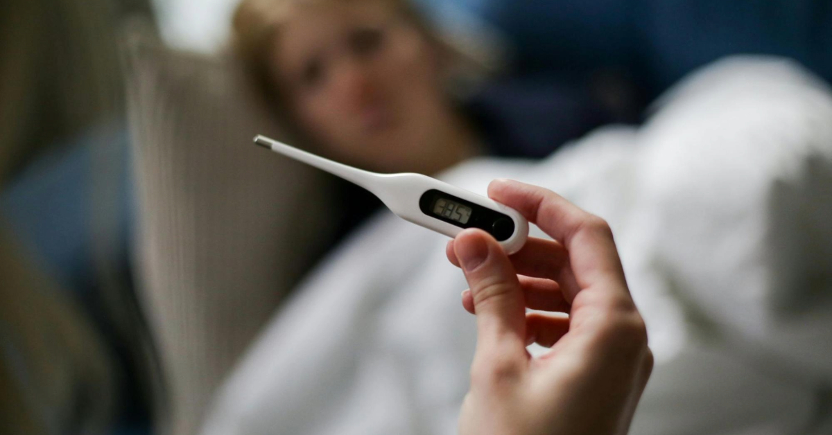 Sick person with a thermometre showing being feverish