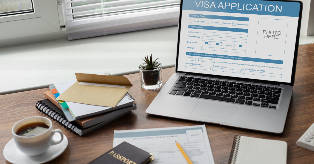 An Irish visa application form opened in laptop with a passport, notebooks, and a cup of tea placed in front of it