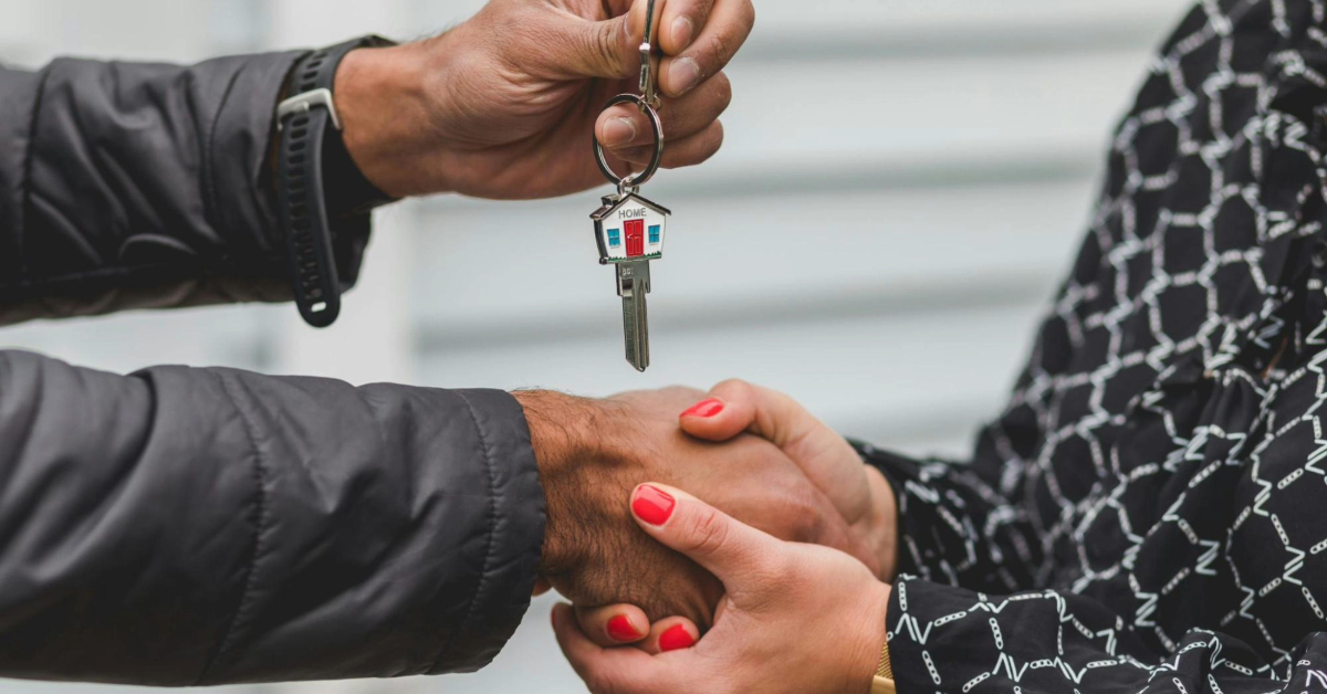 Two people shaking hands and handling a key to a property