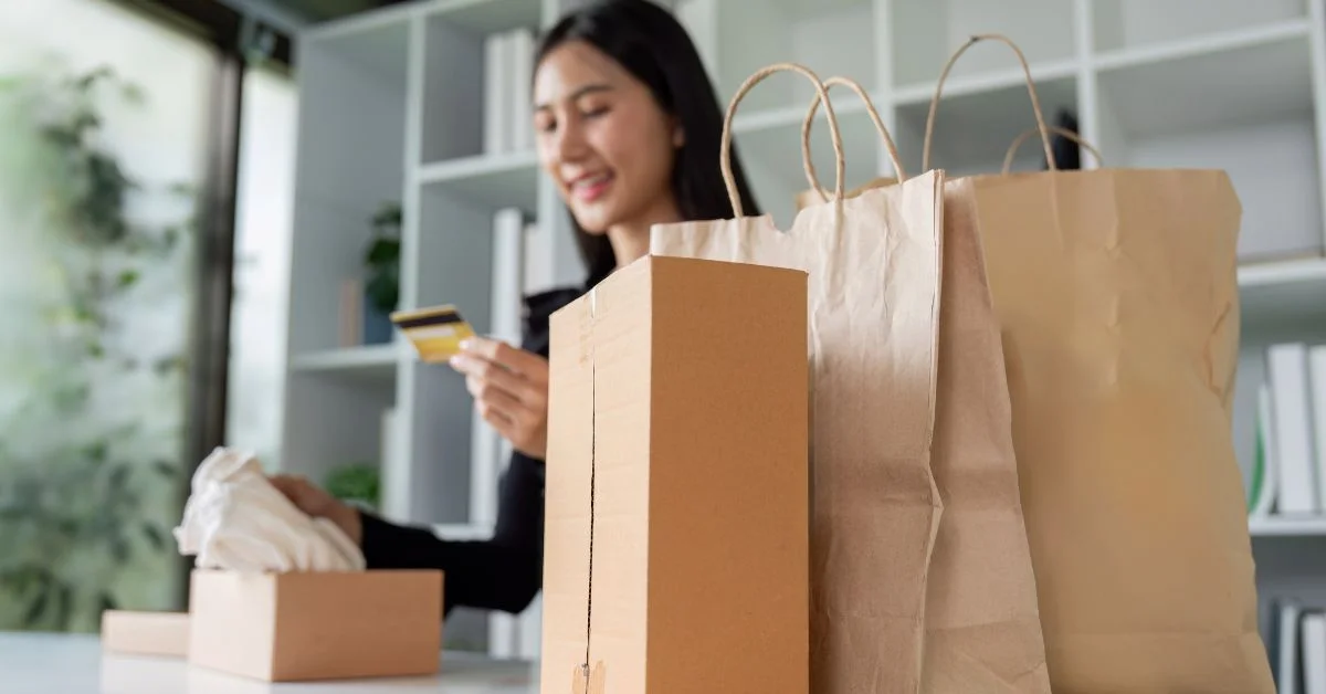 A woman holding her credit card with groceries bag besides her