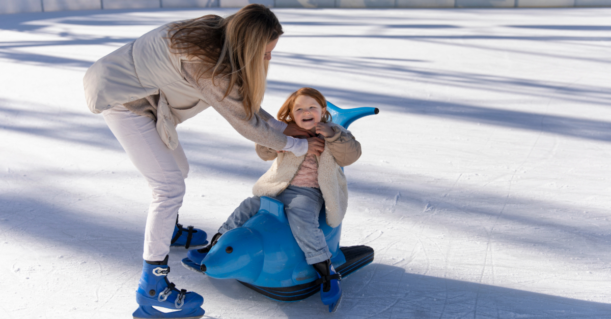 A little girl learns to skate while holding on to the penguin support