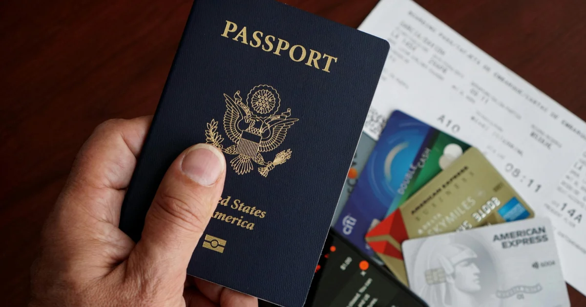 A person holding their passport and visa in their hands while bank cards lie on the table