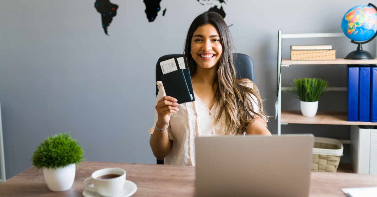 A smiling woman holding her passport and visa with her laptop and tea at the table