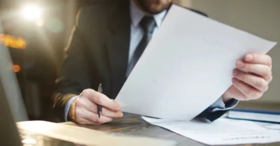 A man sits at his desk with a laptop in front of him, reviewing papers