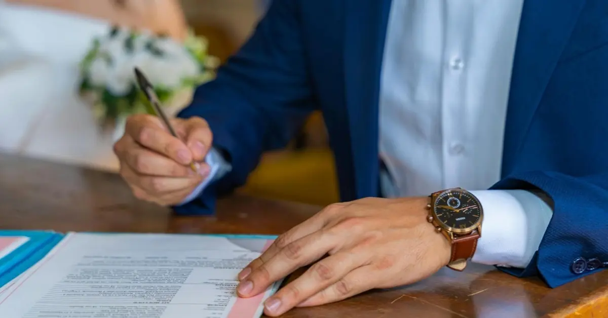 لقطة مقرّبة للعريس وهو يوقع وثائق الزواج والعروس بجانبه.