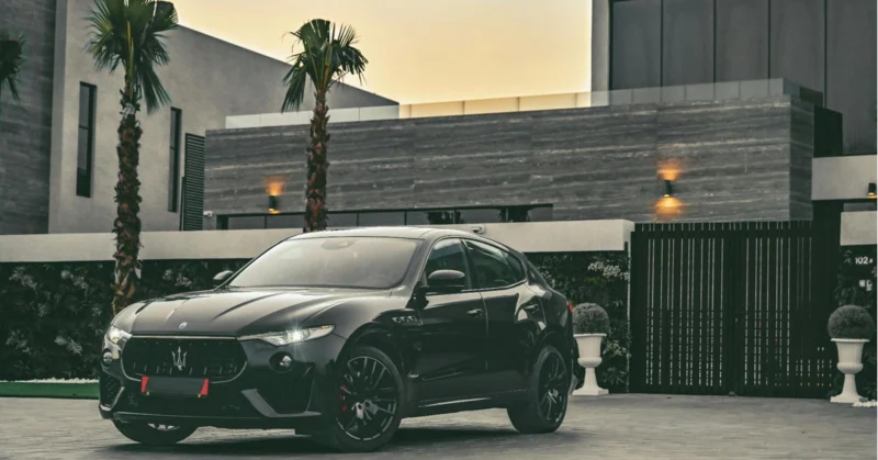 A luxury car parked in front of a modern villa with a clean architectural background.
