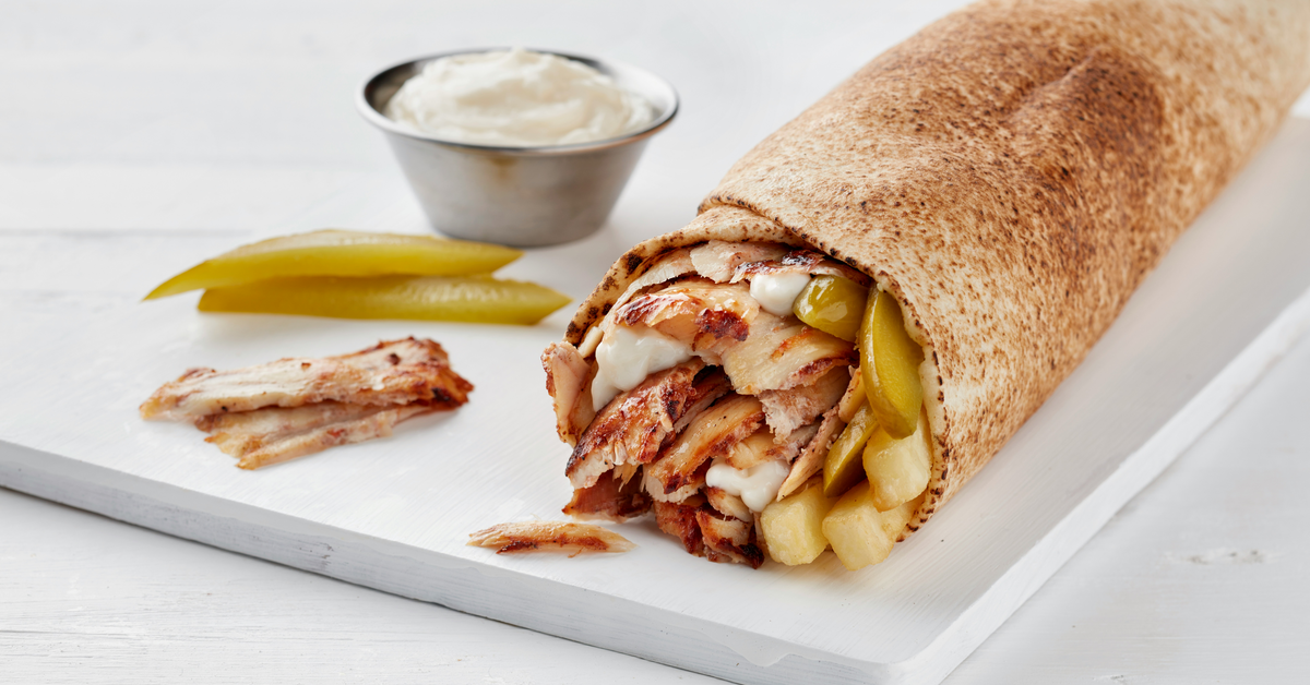 A shawarma with pickles and sauce on the table