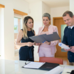 Three professionals discussing documents in a well-lit office space, representing teamwork and collaboration in running a successful real estate agency.