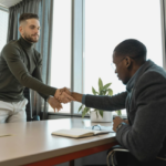 Two business professionals shaking hands across a desk, symbolizing a successful partnership or agreement in a modern office setting, relevant for new real estate agency collaborations in Dubai.