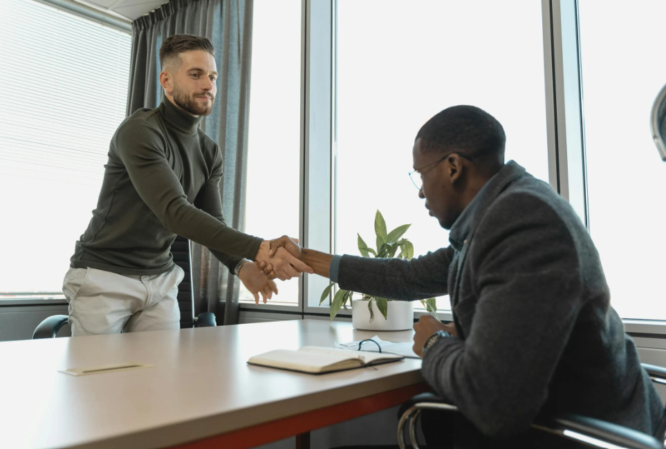 Two business professionals shaking hands across a desk, symbolizing a successful partnership or agreement in a modern office setting, relevant for new real estate agency collaborations in Dubai.