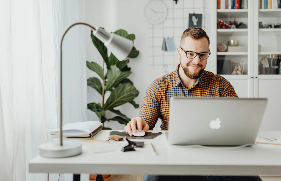 Smiling man working on a laptop in a bright, modern home office, illustrating focus and efficiency, perfect for a blog article on digital productivity tools for real estate professionals.