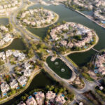 Aerial view of luxury residential clusters surrounded by man-made lakes at Jumeirah Islands in Dubai. The circular and semi-circular neighborhoods feature modern villas with private swimming pools, tree-lined streets, and green spaces. Water fountains and connecting bridges add to the aesthetic of this exclusive community.