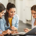 Real estate agent showing documents to a young couple during a client consultation in a modern, brightly lit home.