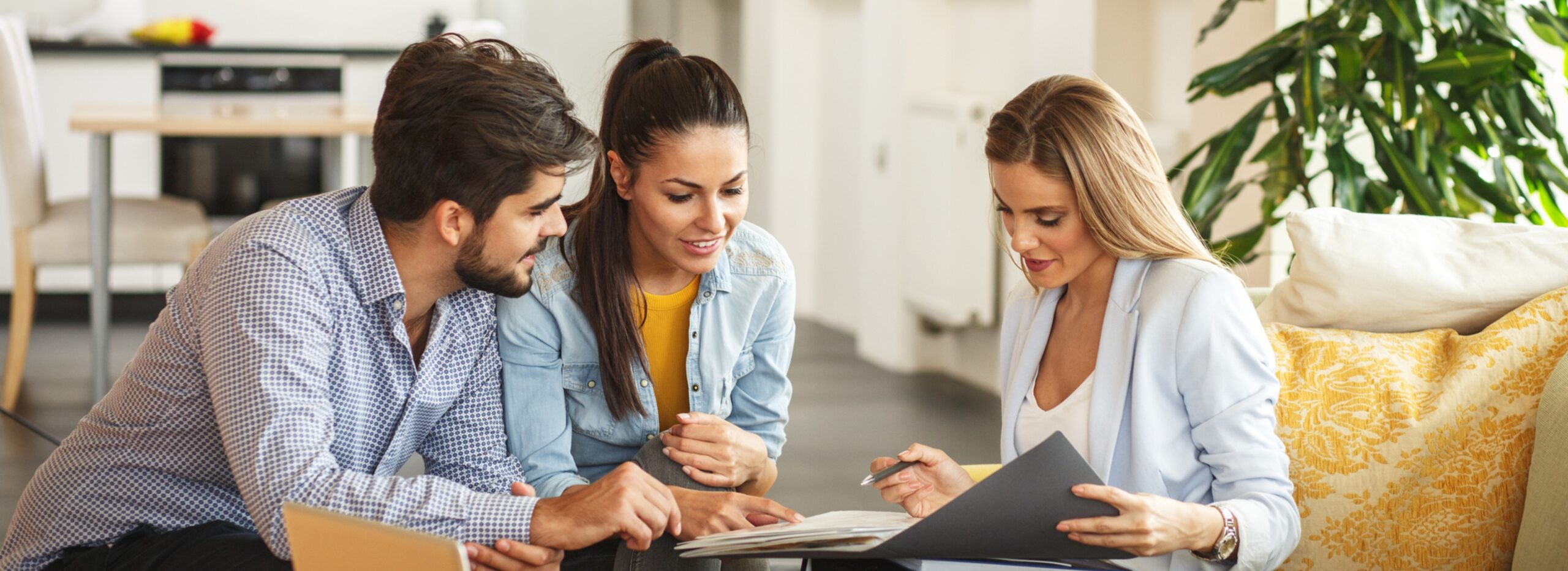 Real estate agent showing documents to a young couple during a client consultation in a modern, brightly lit home.
