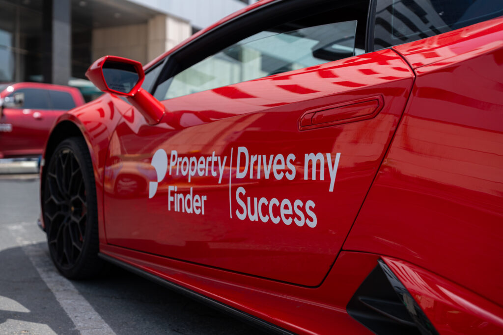 Close-up of a red sports car featuring the Property Finder logo and the slogan 'Drives my Success' on the door, part of a branded activation for top-performing real estate agents in Dubai.