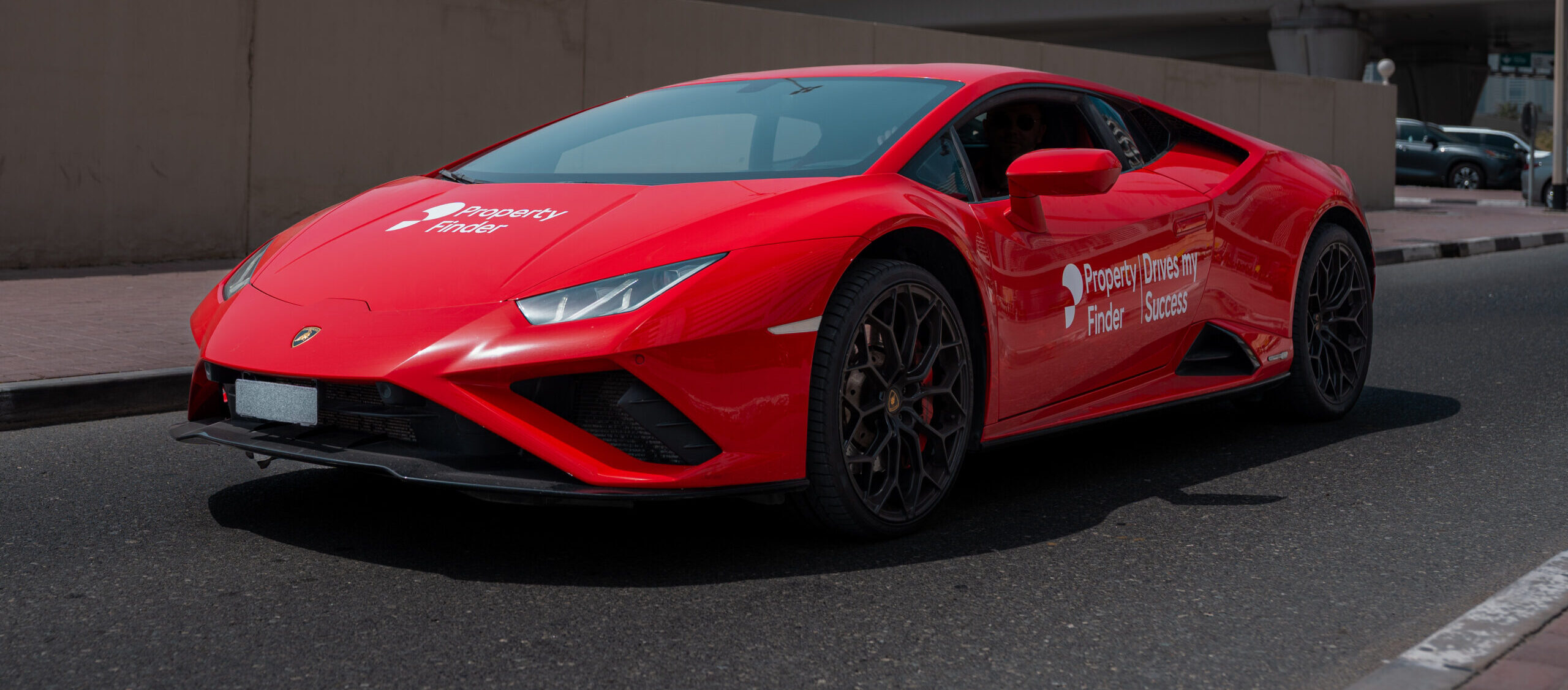 A red Lamborghini sports car branded with Property Finder and the slogan 'Drives my Success,' photographed on a Dubai street during the SuperAgent recognition event.