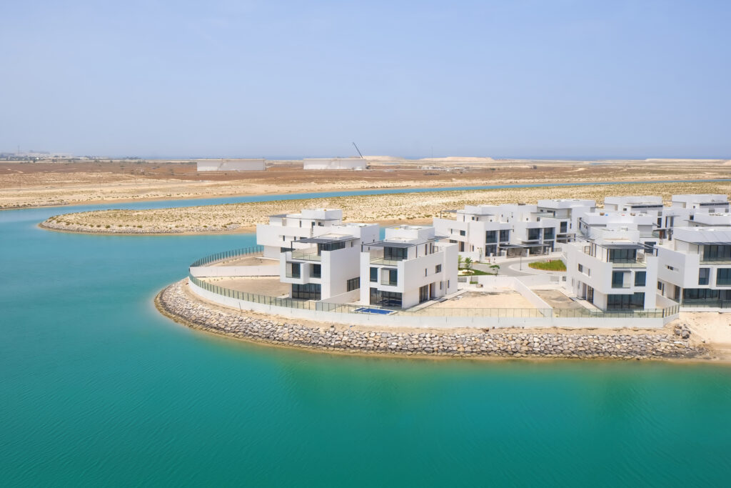 Modern white villas overlooking a turquoise waterfront in Abu Dhabi, showcasing luxury ready-to-move-in properties in a desert coastal development.