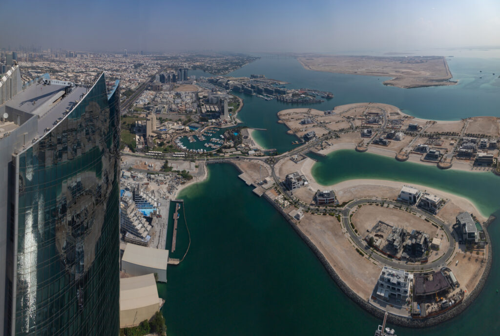 Aerial view of Abu Dhabi’s Al Gurm coastal district with luxury waterfront villas, man-made islands, and high-rise buildings reflecting in the Arabian Gulf.