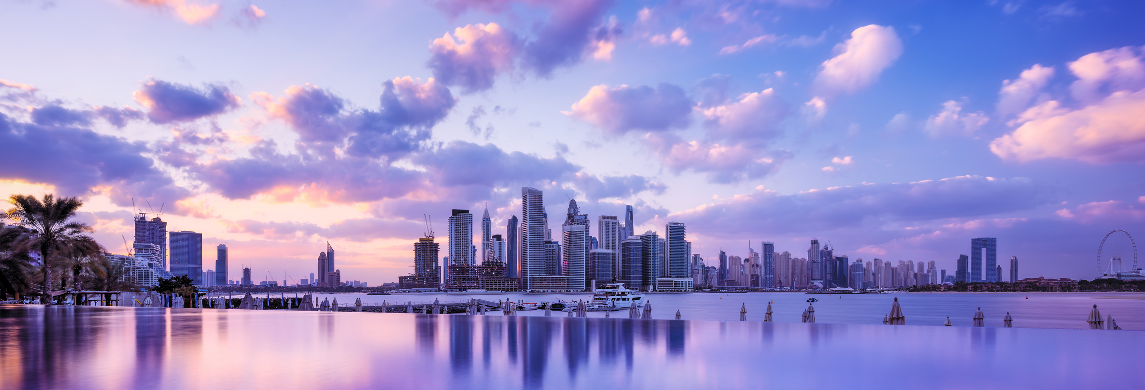 Panoramic view of Dubai Marina skyline at sunset, with vibrant clouds reflecting in calm waterfront, showcasing the city’s luxury real estate landscape.