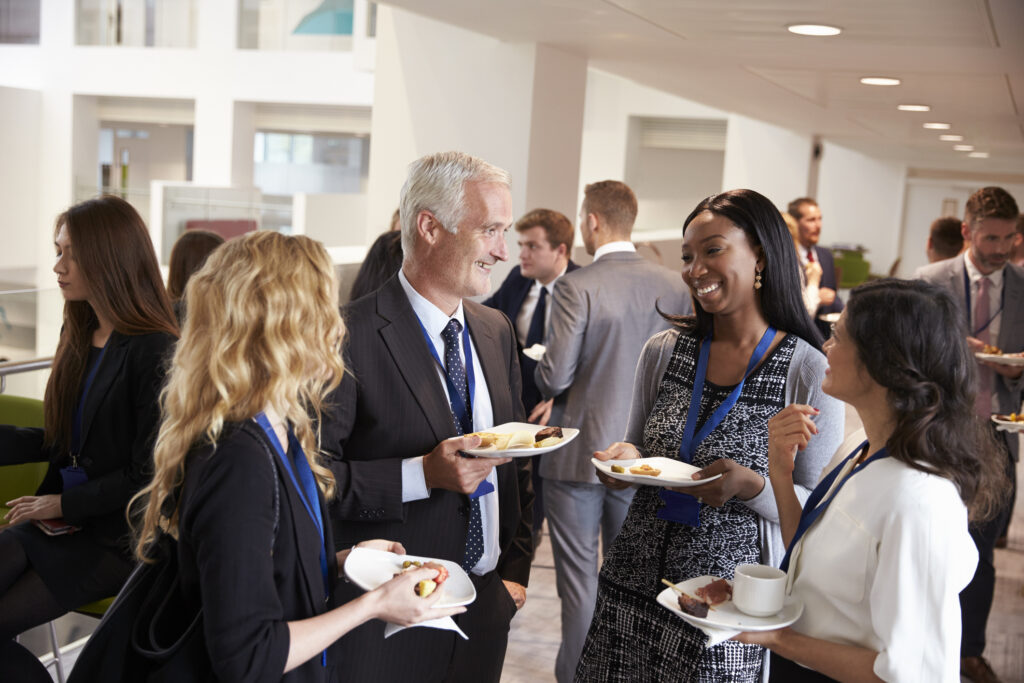 Group of real-estate professionals mingling over coffee and canapés at a conference reception, illustrating how informal networking builds valuable industry connections.
