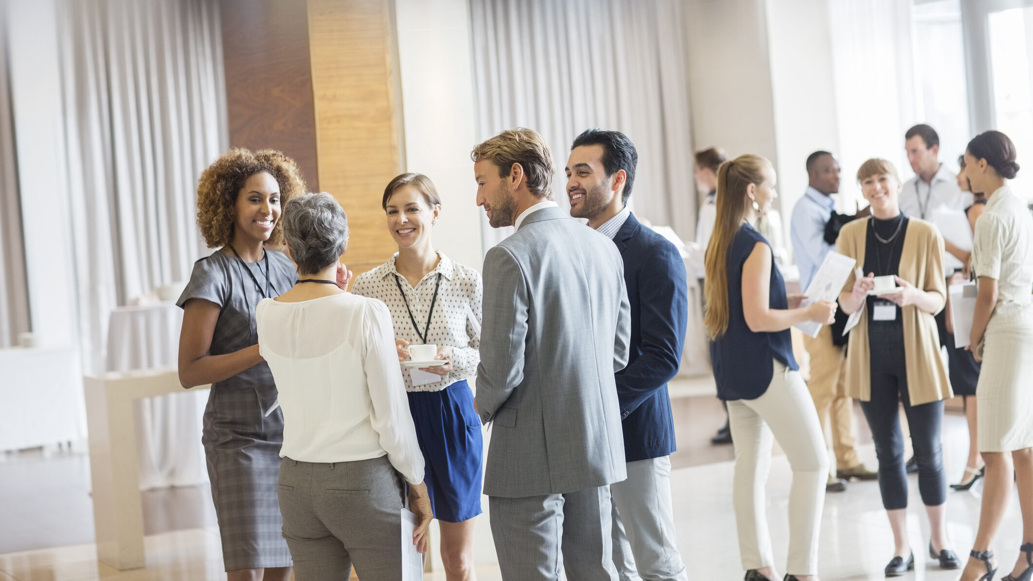 Real estate professionals networking and conversing in a bright, modern event space during a business conference—illustrating the value of industry events for talent recruitment and relationship-building.