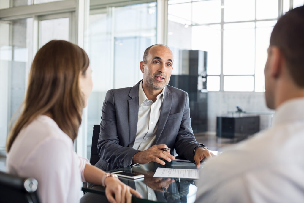 A professional estate agent attentively listening and advising a couple across the table, illustrating personalised client engagement in a modern office setting.