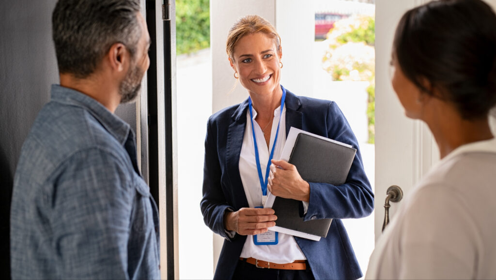 Smiling real estate agent greeting a couple at their front door for their first face-to-face meeting.