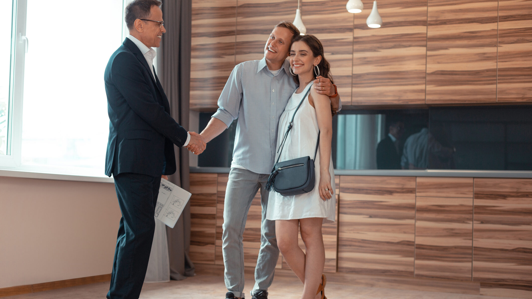 Happy couple receiving keys and shaking hands with real estate agent at off-plan property handover in Dubai.