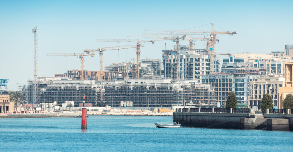 Waterfront view of new off-plan real estate development under construction in Dubai with cranes and modern buildings.