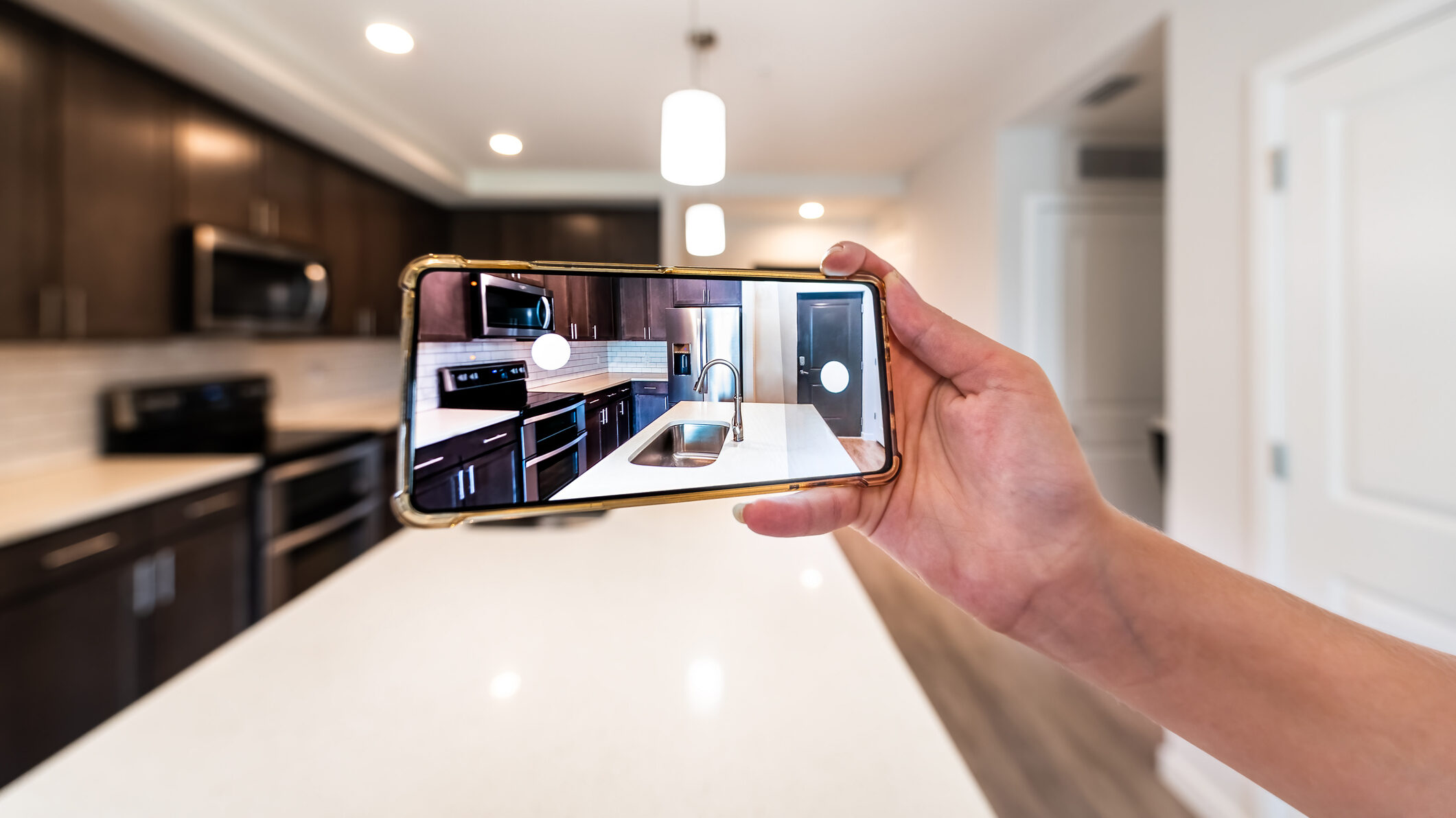 Real estate agent filming home tour on their phone to show a house apartment kitchen island room for sale or rent tour with phone smartphone closeup point of view in modern luxury condo home with blurry bokeh background