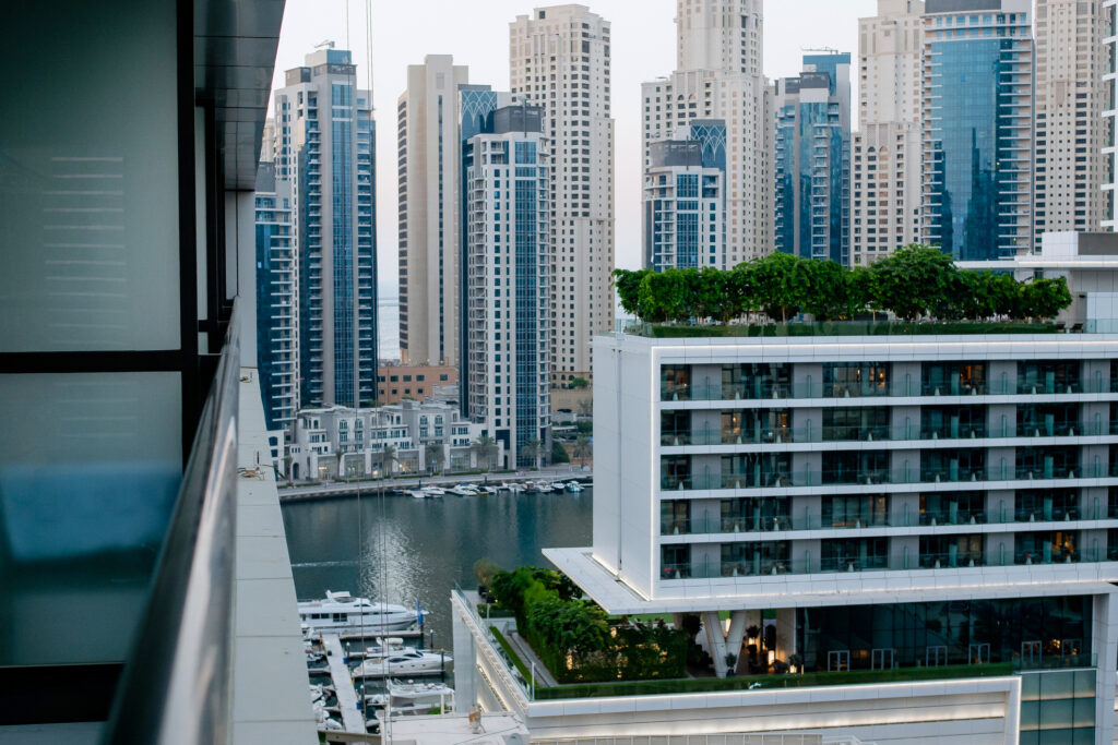 Modern residential towers and waterfront apartments in Dubai Marina, highlighting opportunities in off-plan real estate sales. View from the balcony of high-rise buildings and a water channel with boats. Business center