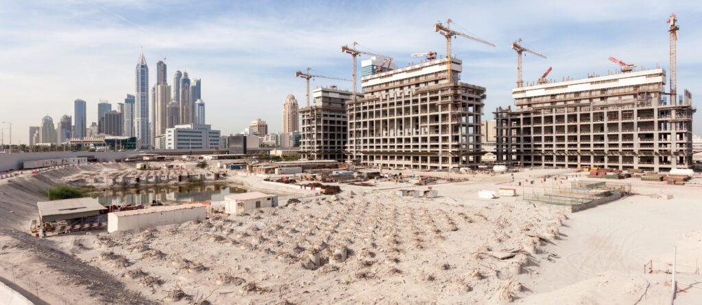 Construction site of new off-plan real estate development in Dubai with cranes and high-rise towers in the background.