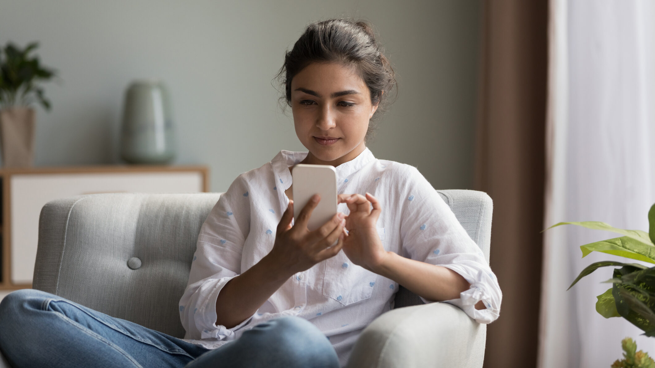 Young woman sitting at home using a smartphone, representing a UAE real estate buyer who has opted in to WhatsApp updates, highlighting the importance of permissioned contact lists and targeted messaging.