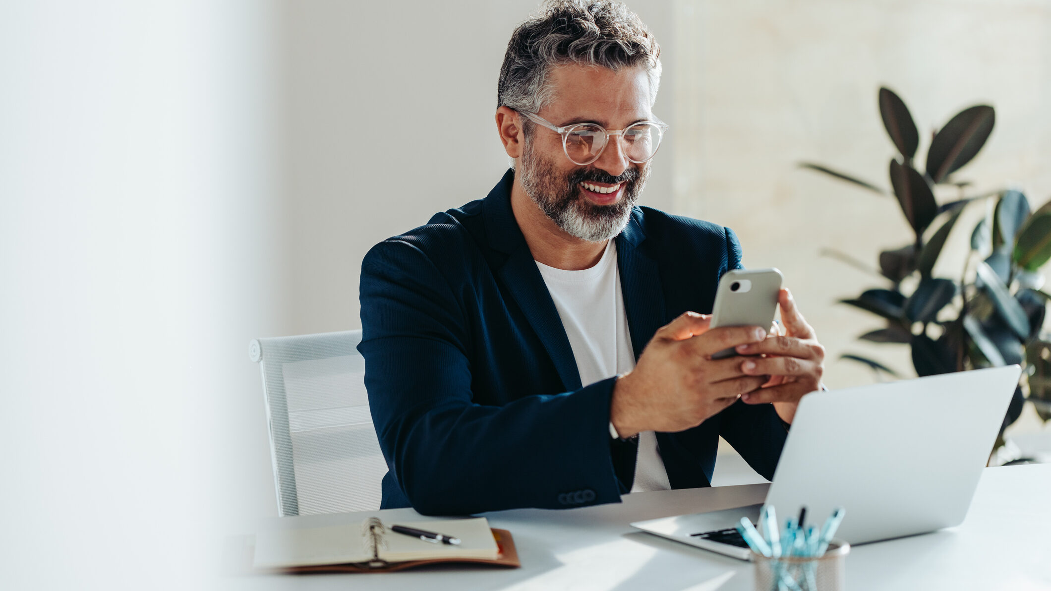 Smiling real estate agent using WhatsApp on a smartphone at a modern office desk with a laptop, illustrating how UAE property professionals use mobile messaging to boost lead conversion, build trust, and respond to buyers quickly.