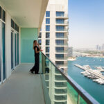 New tenant standing on high-rise balcony of a new Build to Rent building overlooking Dubai Marina waterfront with yachts, blue water and city skyline in the distance