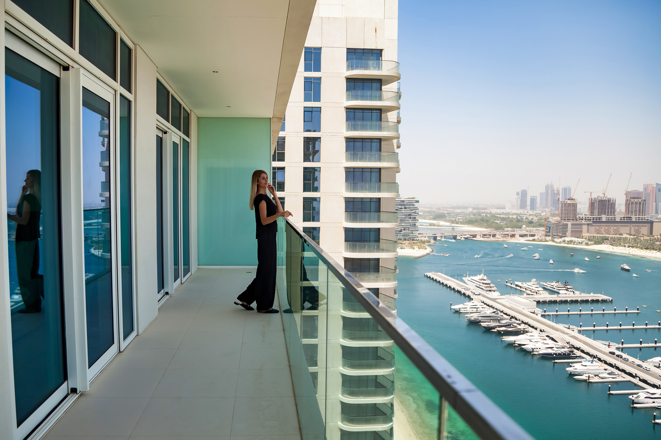 New tenant standing on high-rise balcony of a new Build to Rent building overlooking Dubai Marina waterfront with yachts, blue water and city skyline in the distance