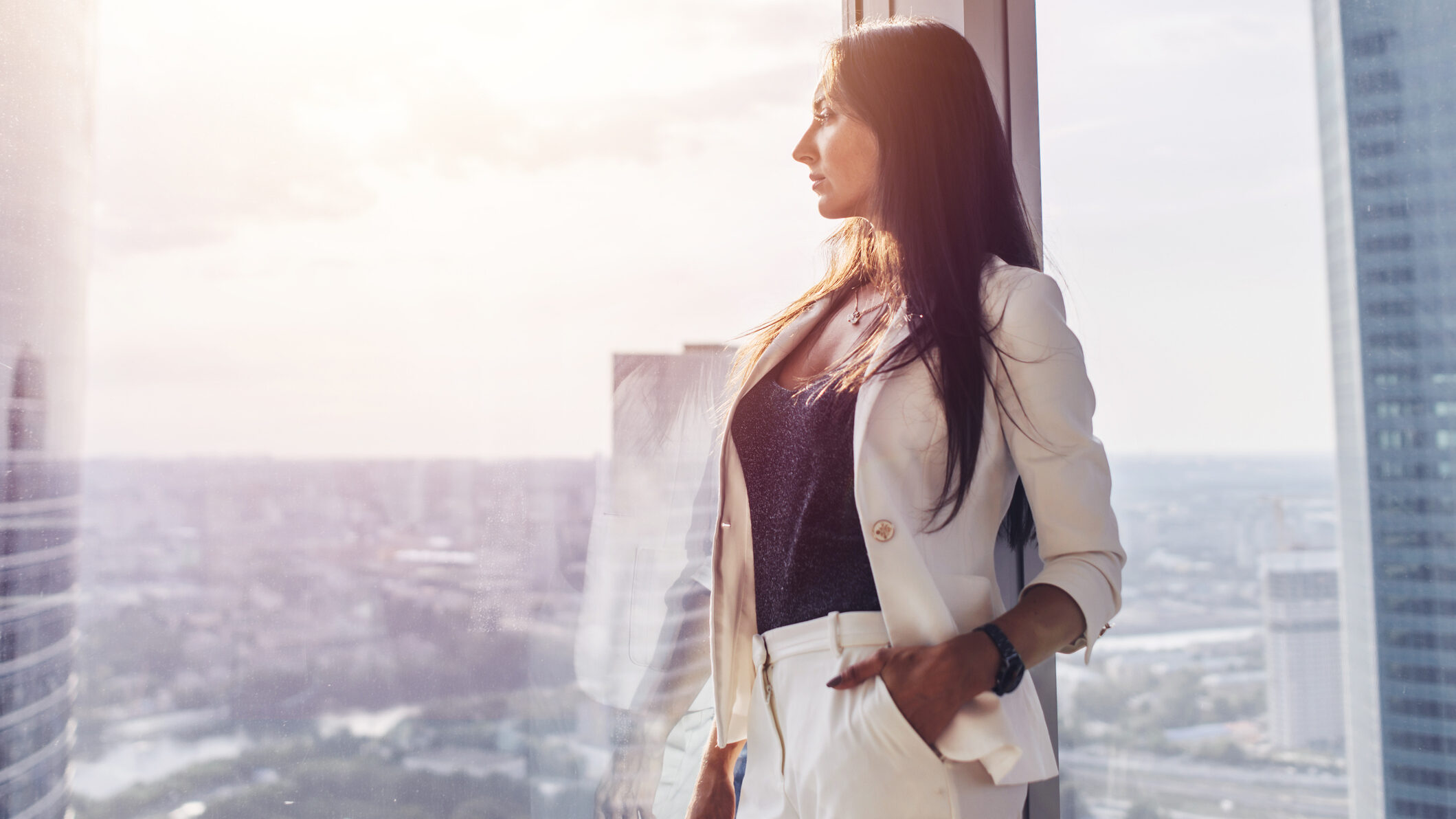 Real estate agent standing by a high-rise window overlooking a modern city skyline for personal brand photography in Dubai - perfect for Instagram.