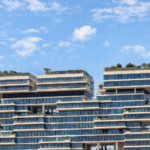 Modern luxury residential building with tiered architecture, rooftop gardens, and energy-efficient glass façades under a blue sky, showcasing sustainable real estate design in Dubai.